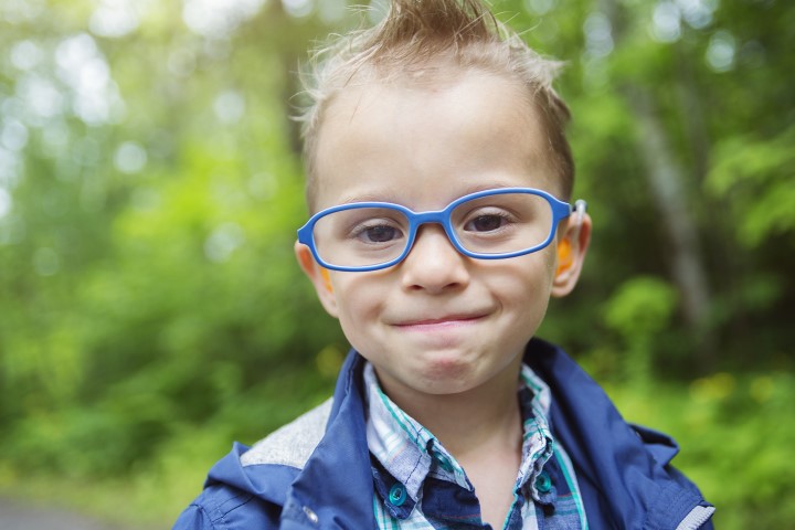 Young boy wearing glasses, smiling at the camera.